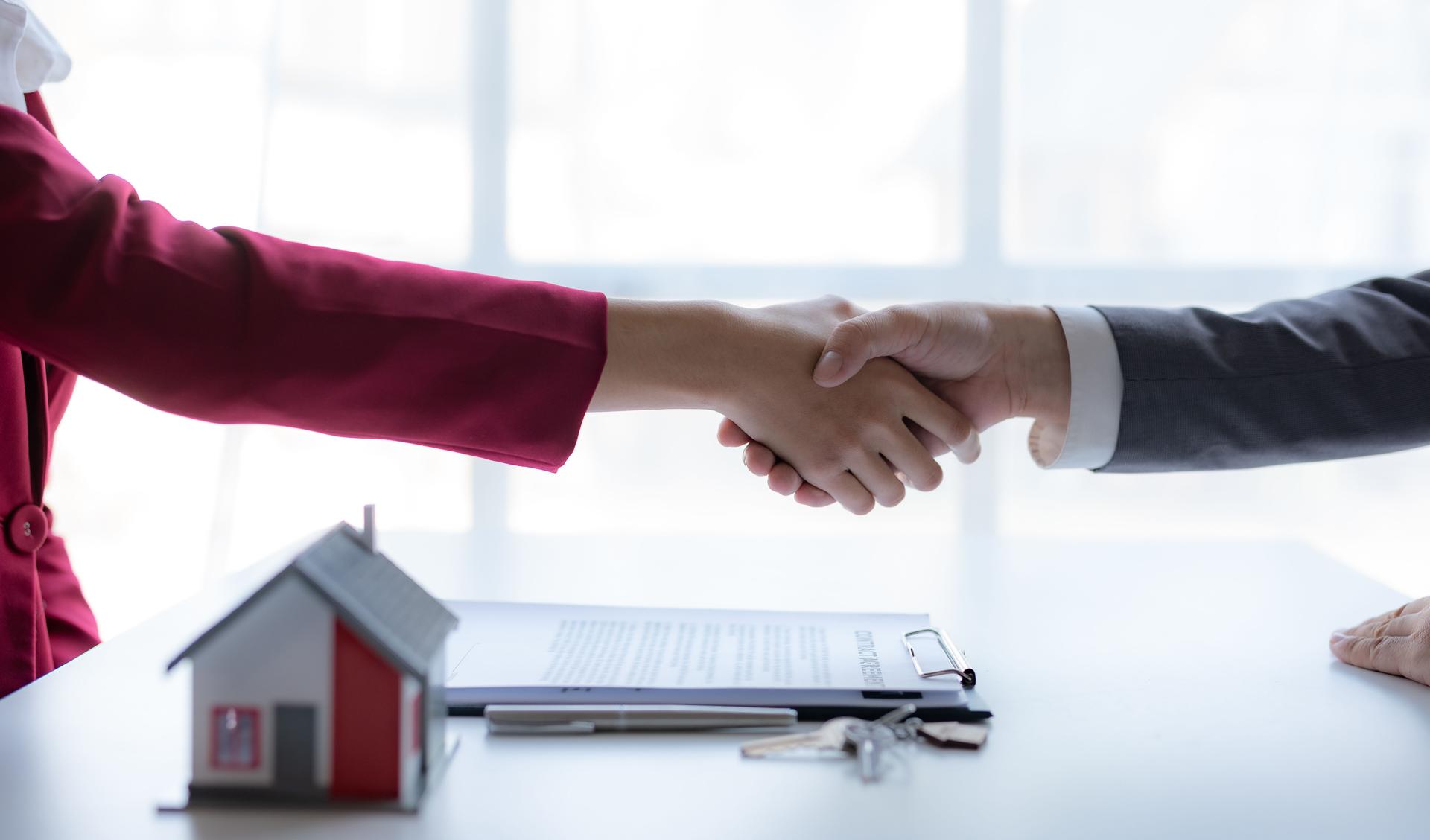 Immobilienmakler schüttelt einem Kunden die Hand, um einen Hauskaufvertrag zu unterzeichnen und dem Kunden zu gratulieren.